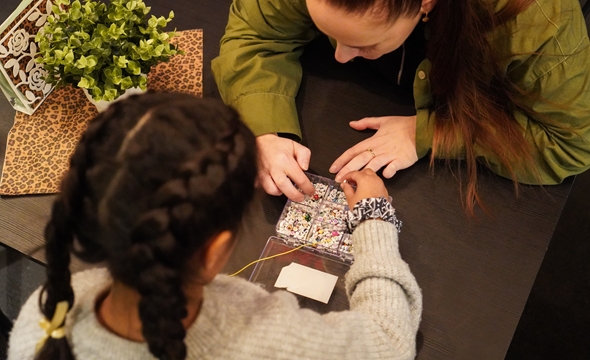 En frivillig fra Røde Kors og en jente sitter ved et bord og perler