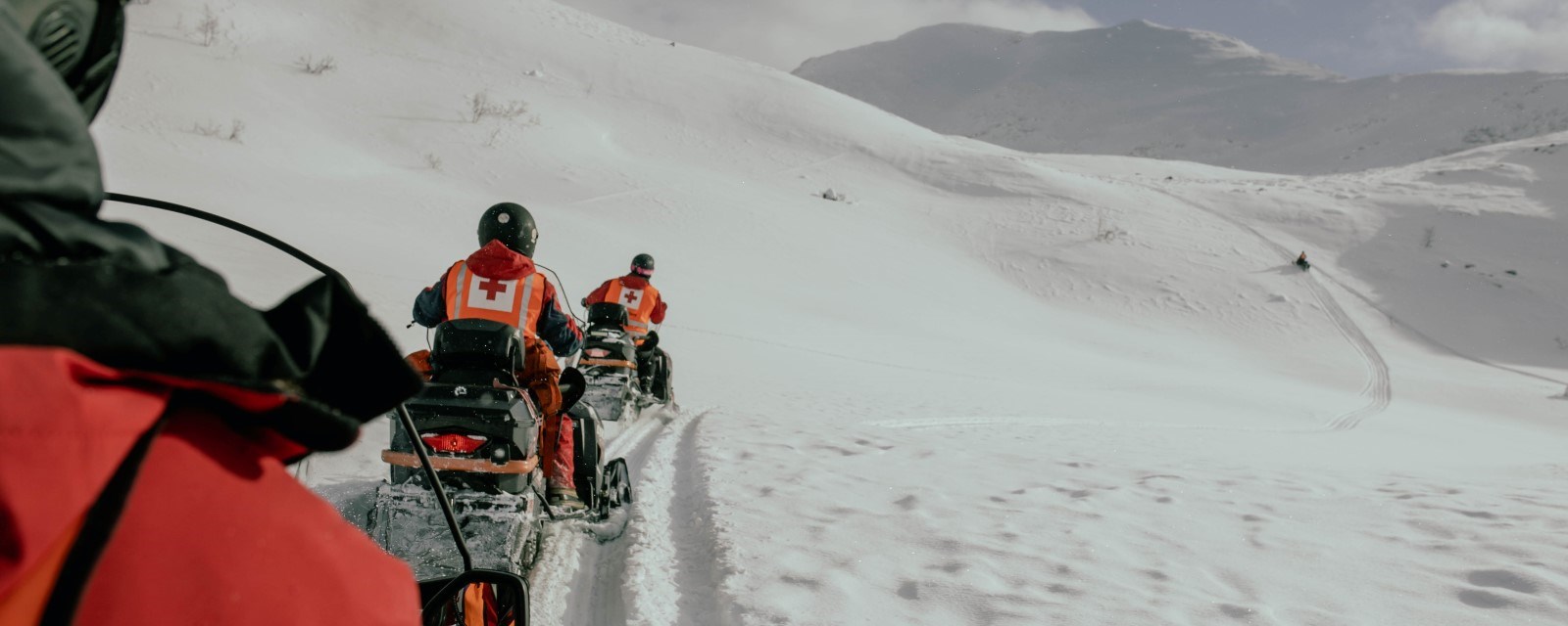 Teams from the Red Cross search and rescue driving snowmobiles in the mountains