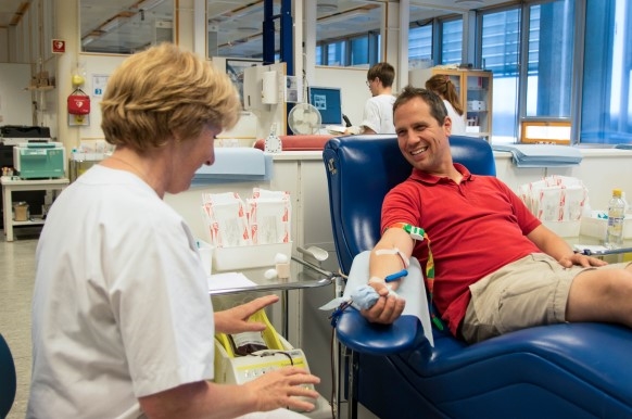 En mann sitter i en stol og gir blod. En kvinnelig sykepleier sitter sammen han og følger med.