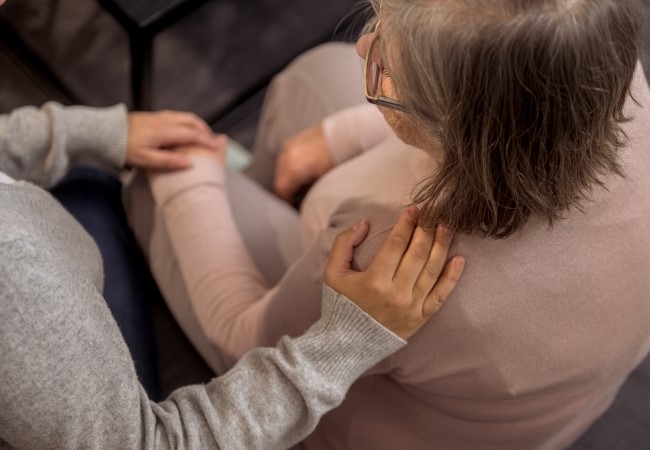 En kvinne holder en hånd på skulderen til en eldre kvinne som er ensom.