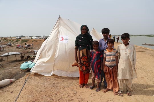 En mor og hennes 4 barn står utenfor et nødtelt fra IFRC, flom