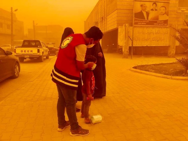 En mann fra Irak Røde Halvmåne tar munnbind på en liten jente i en sandstorm.