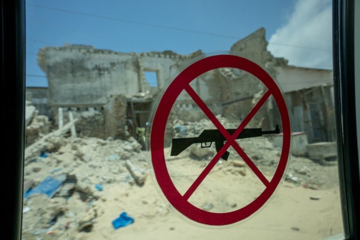 En vindu med et "våpen forbudt" klistremerke, på utsiden ser man en utbombet by.