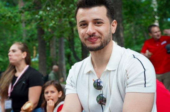 A man sits in a park in summertime. He participates at a Red Cross event.