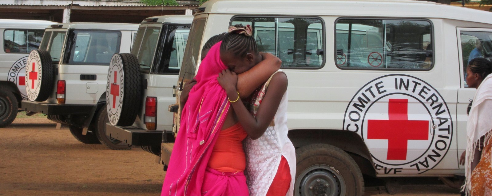 To kvinner står foran en bil fra Røde Kors og holder rundt hverandre.