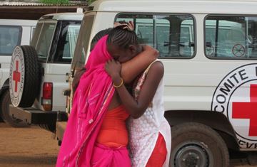 To kvinner står foran noen bilder fra Røde Kors og holder rundt hverandre.