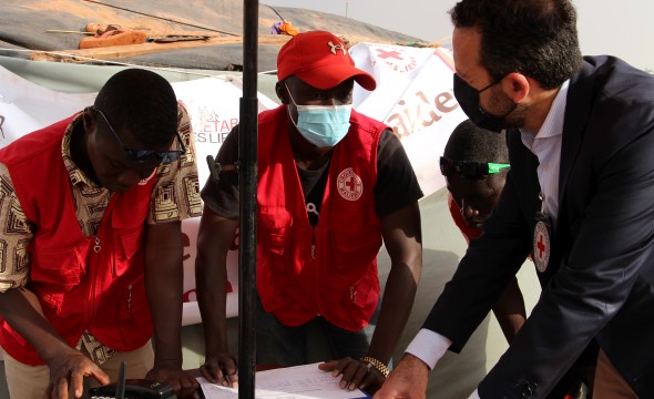 Tre menn fra Røde Kors ser på noen papirer på et bord.